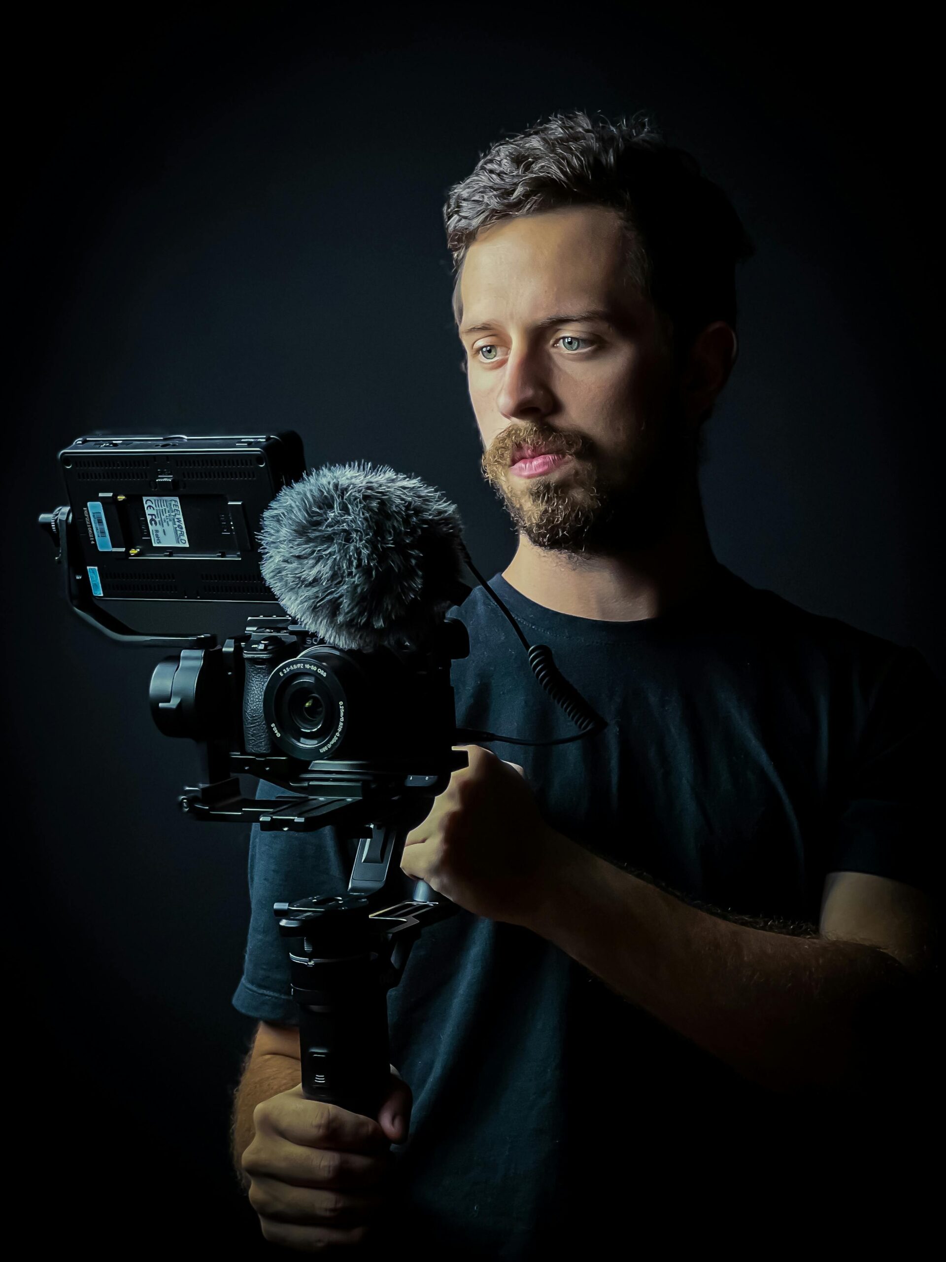 A bearded videographer holding a camera rig during a studio photoshoot.